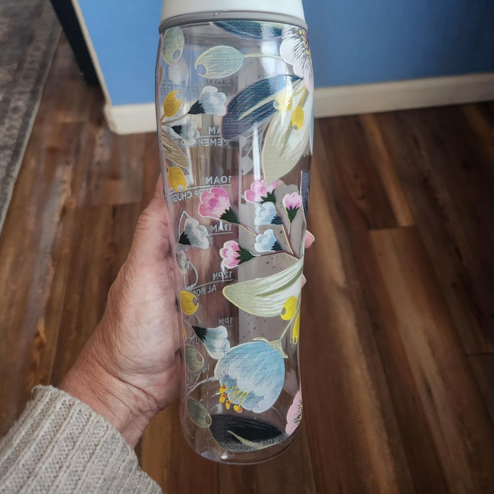 Hand holding a floral-patterned water bottle indoors.