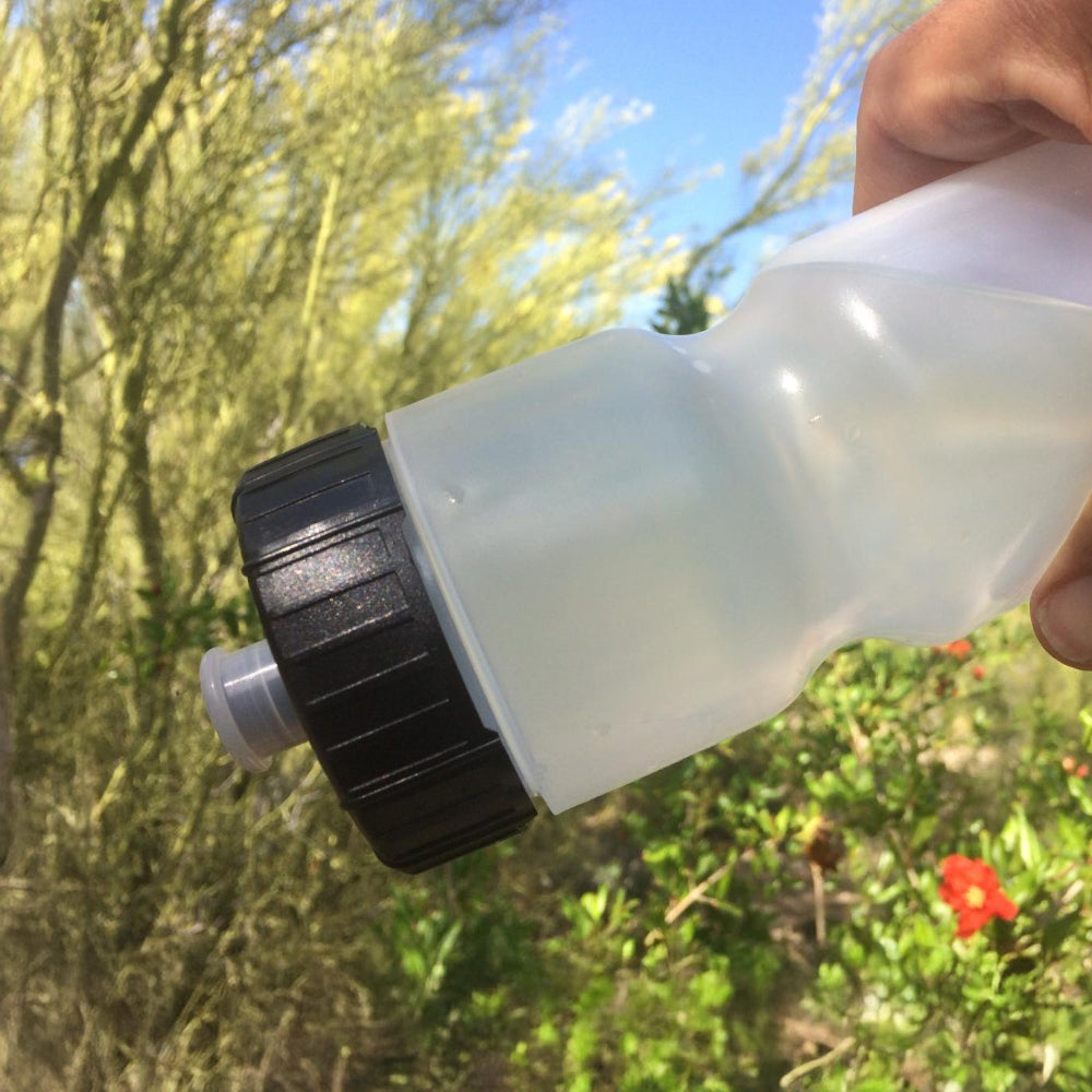 Hand holding a white spray nozzle and black top against a natural background