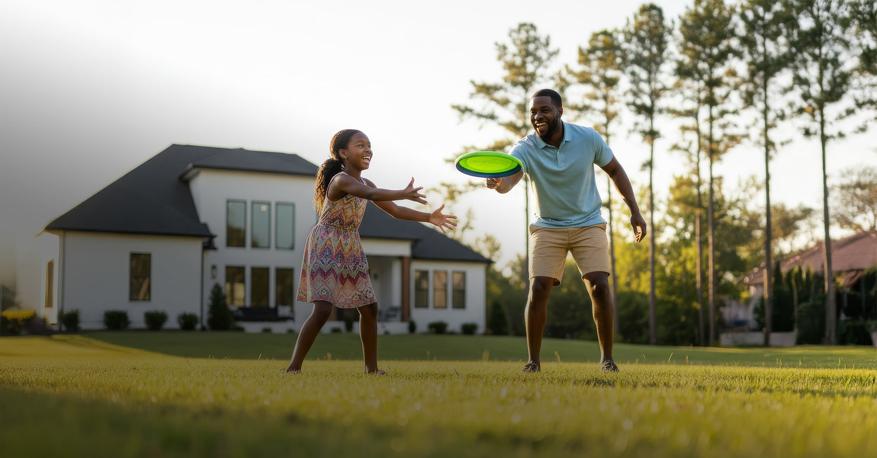 Man and young girl playing with a frisbee in a grassy yard with a house in the background.