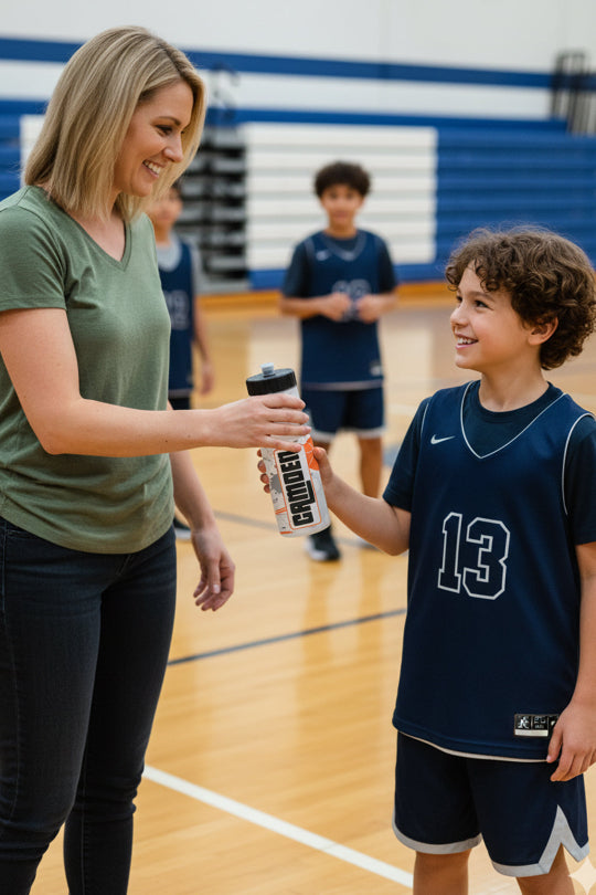 Woman handing a water bottle to a young boy on a basketball court