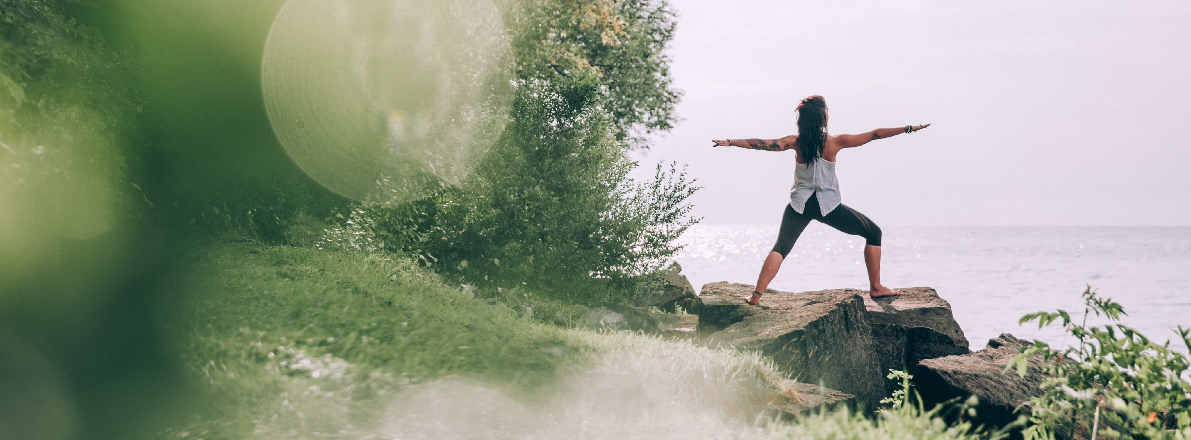 Person practicing yoga on a rock by a body of water with trees in the background